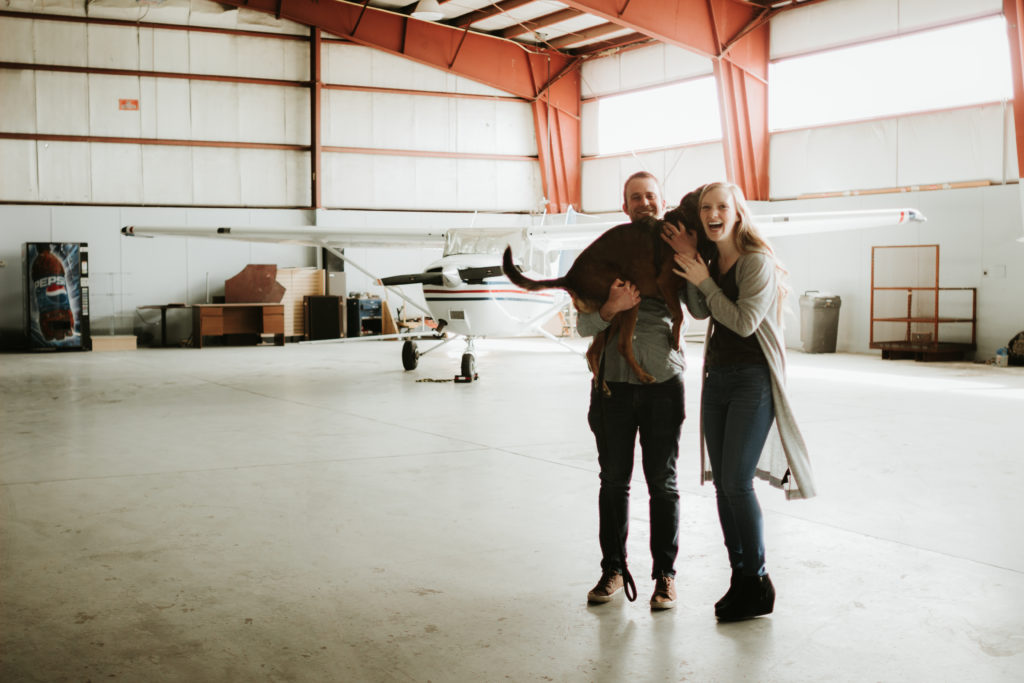couple and dog in front of small plane
