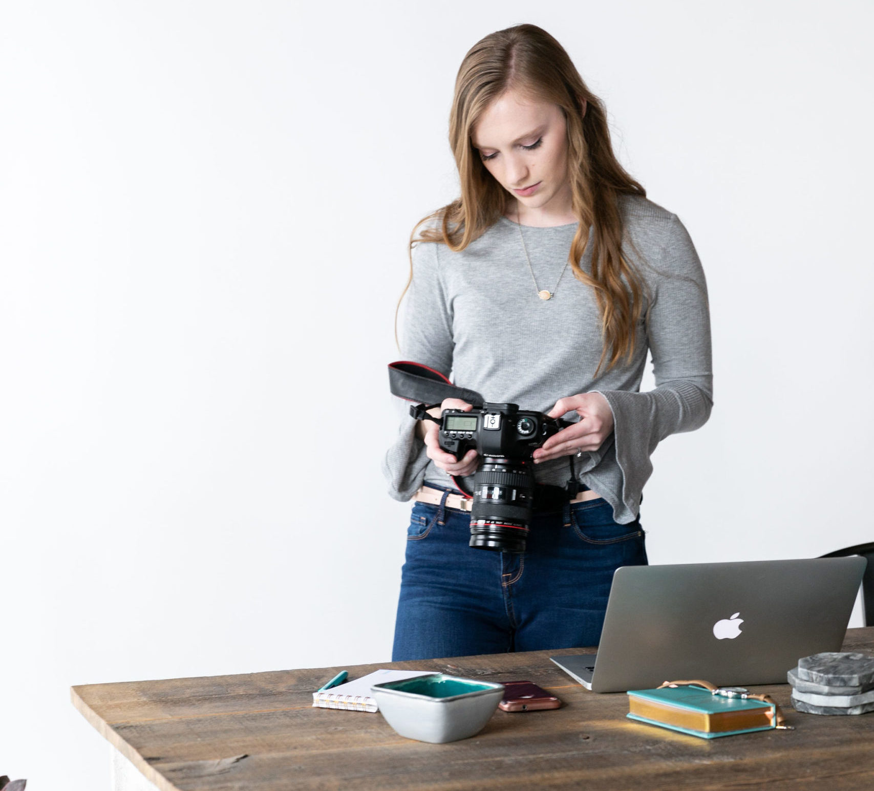 Woman in a gray shirt stands over a desk with a DSLR camera