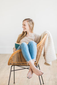 Small business owner reads a book in a wicker chair with her legs up